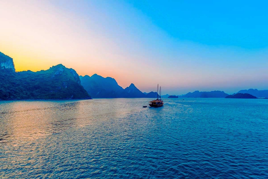 Traditional wooden boat sailing at sunrise on peaceful Halong Bay seascape